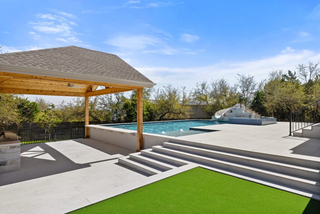Wide view of Stratus Grove outdoor living space with cedar pavilion, geometric pool, water slide, and putting green, Wild Basin Pools Austin TX