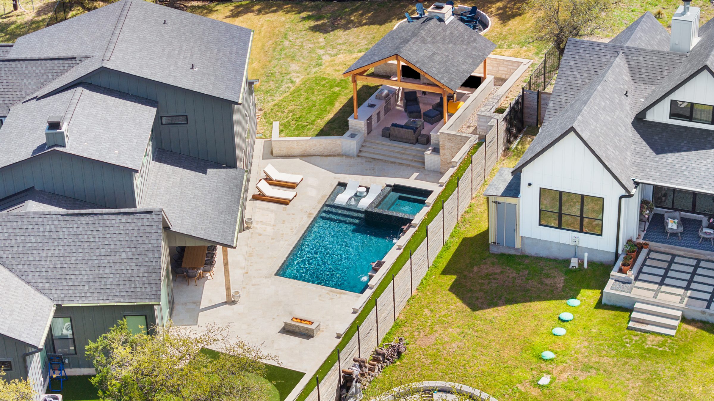 Aerial overview of The Commons backyard featuring a geometric pool, outdoor kitchen pavilion, fire pit, and putting green by Wild Basin Pools Austin TX