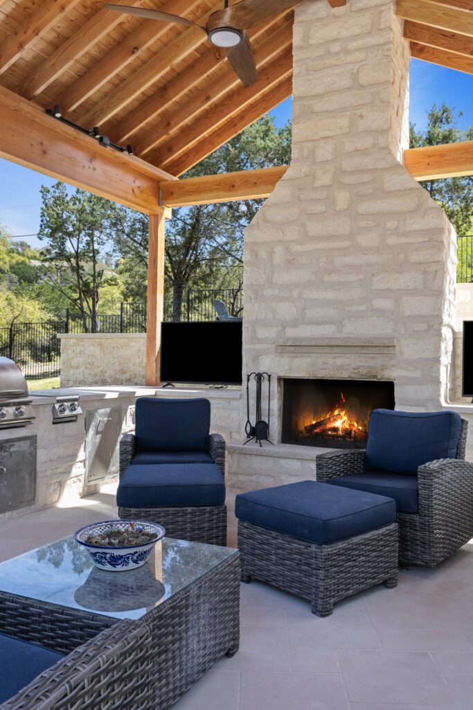 Covered pavilion lounge with lit stone fireplace, cedar ceiling, and navy blue seating at The Commons by Wild Basin Pools Austin TX