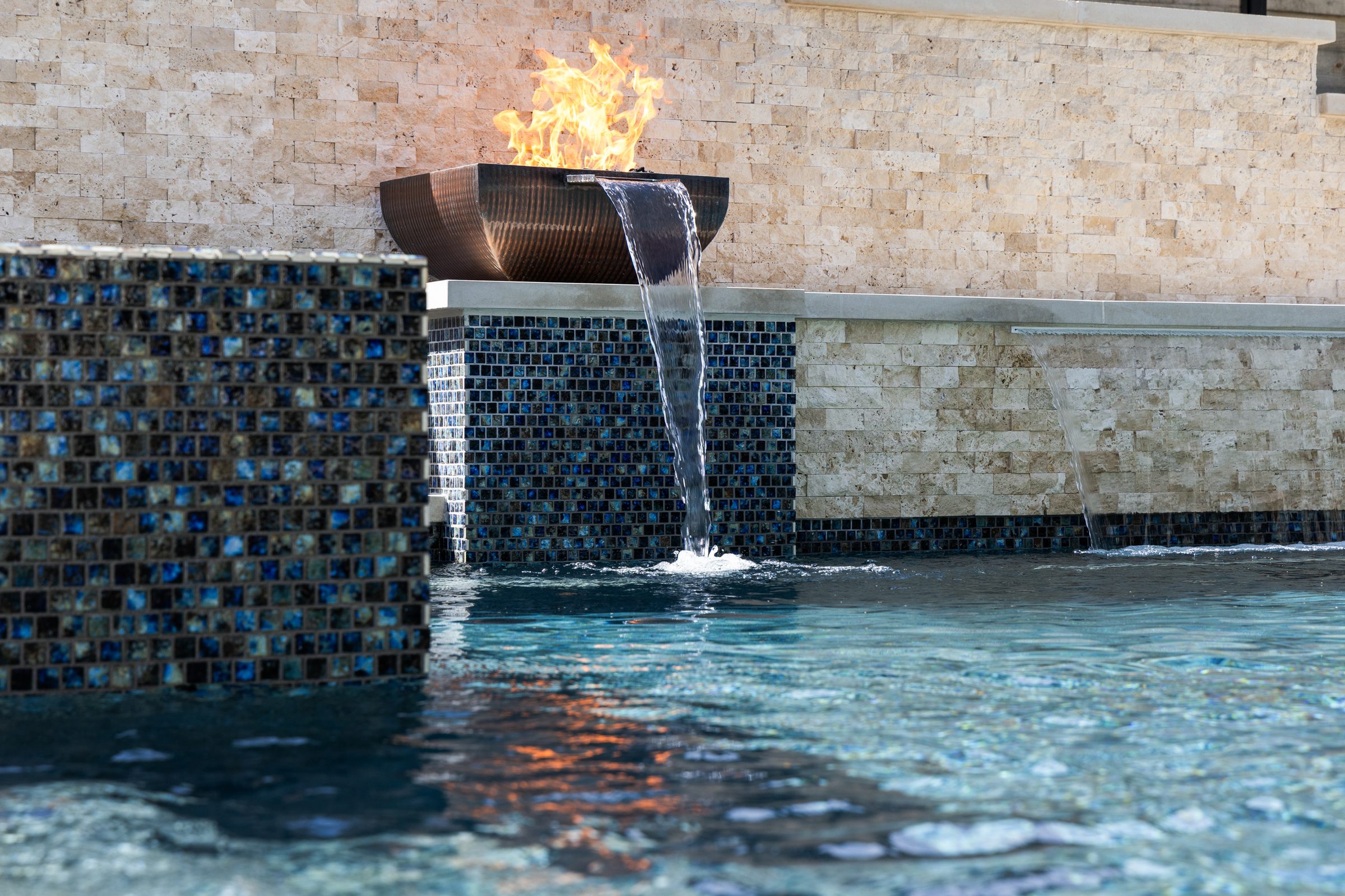 Close up of copper fire bowl and cascading waterfall over iridescent mosaic tile at The Commons pool by Wild Basin Pools Austin TX