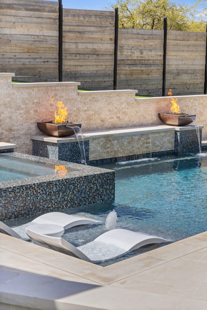 Copper fire bowl with cascading waterfall and tanning ledge loungers at The Commons pool by Wild Basin Pools Austin TX