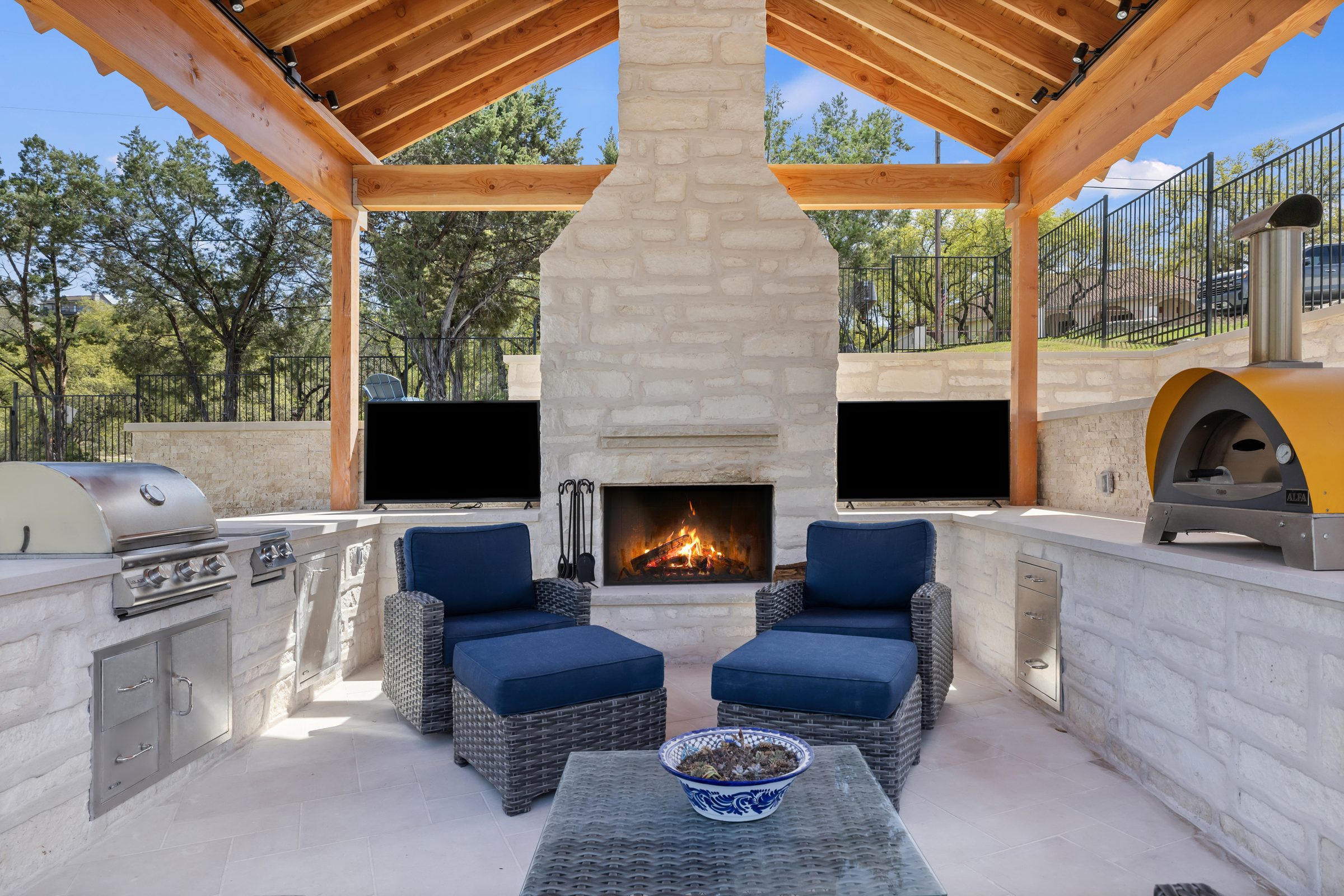 Full outdoor kitchen pavilion at The Commons featuring stone fireplace, built-in grill, pizza oven, and lounge seating by Wild Basin Pools Austin TX
