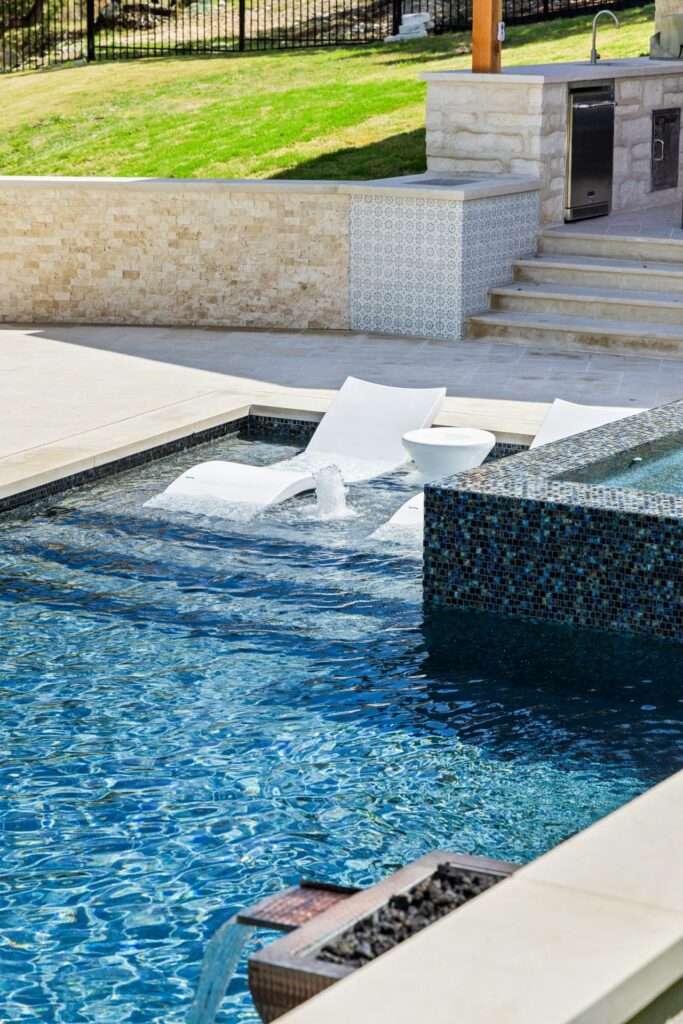 Water level view of The Commons pool with copper fire bowl waterfall and stone fire pit glowing on the patio by Wild Basin Pools Austin TX