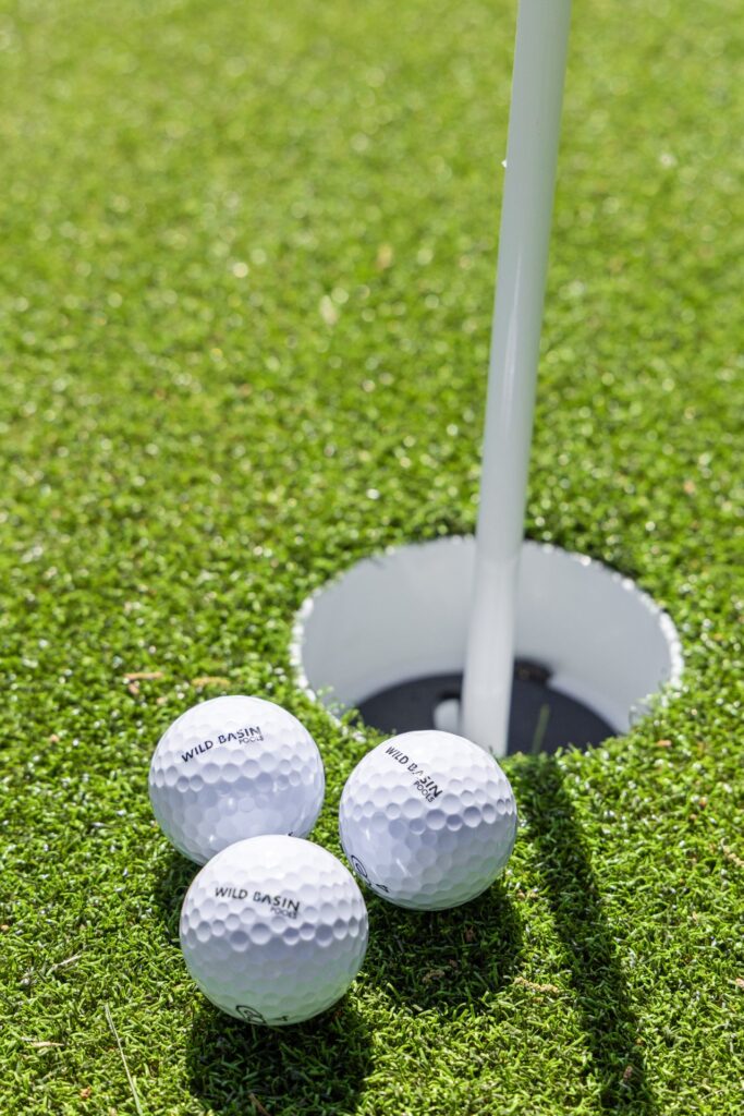 Wild Basin Pools branded golf balls beside the cup on The Commons backyard putting green Austin TX