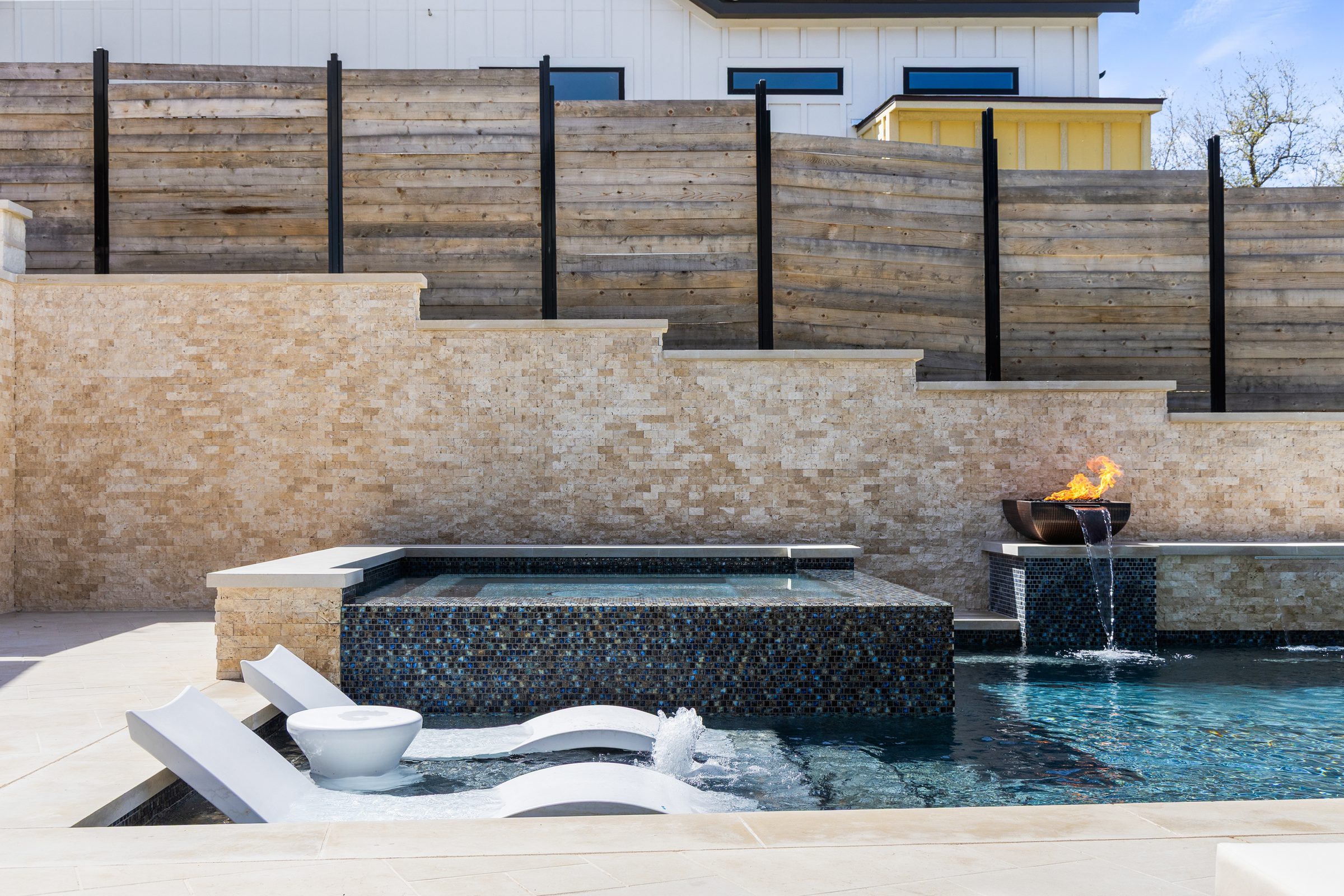 Raised mosaic tiled spa with tanning ledge and copper fire bowl waterfall at The Commons pool by Wild Basin Pools Austin TX