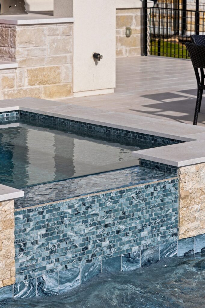Swirled blue-green glass mosaic tile on spa spillover wall with cascading water, Wild Basin Pools Austin TX