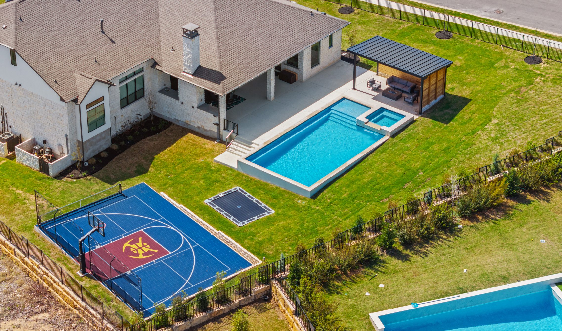 Overhead drone shot of The Backyard Club backyard featuring geometric pool, basketball court and in-ground trampoline by Wild Basin Pools Austin TX