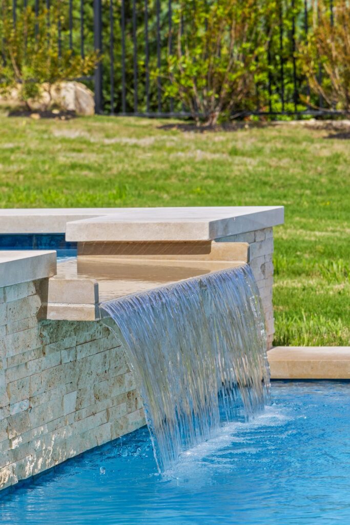 Close up of spa spillover waterfall with travertine stone veneer detail at The Backyard Club Wild Basin Pools Austin TX
