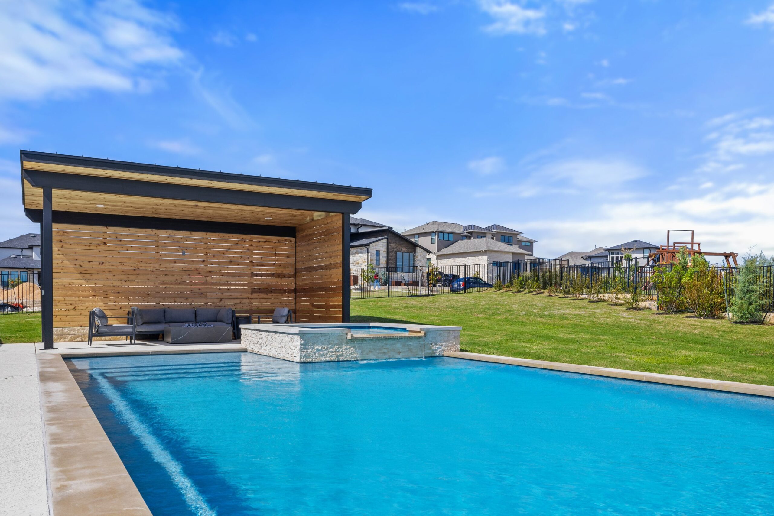 Eye level view of The Backyard Club pool spa waterfall spillover and lounge cabana by Wild Basin Pools Austin TX